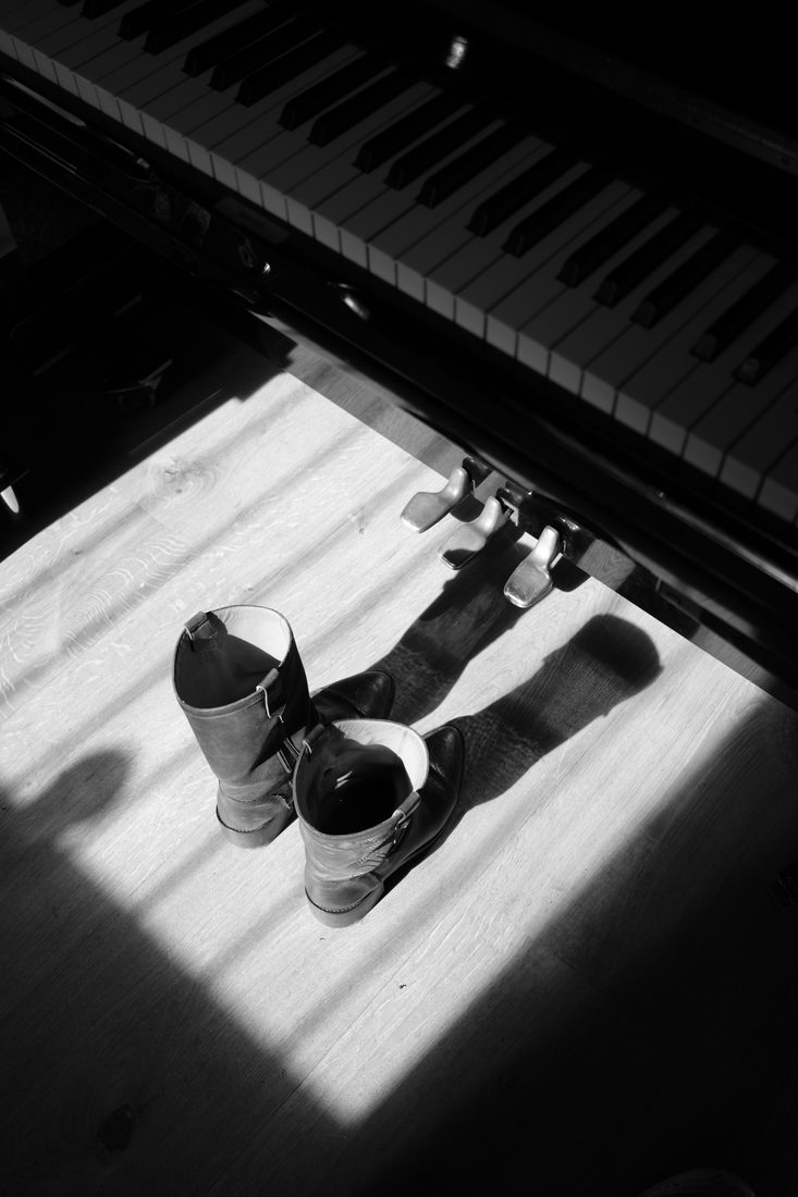 Des bottes posées sous un piano, dans un rai de lumière