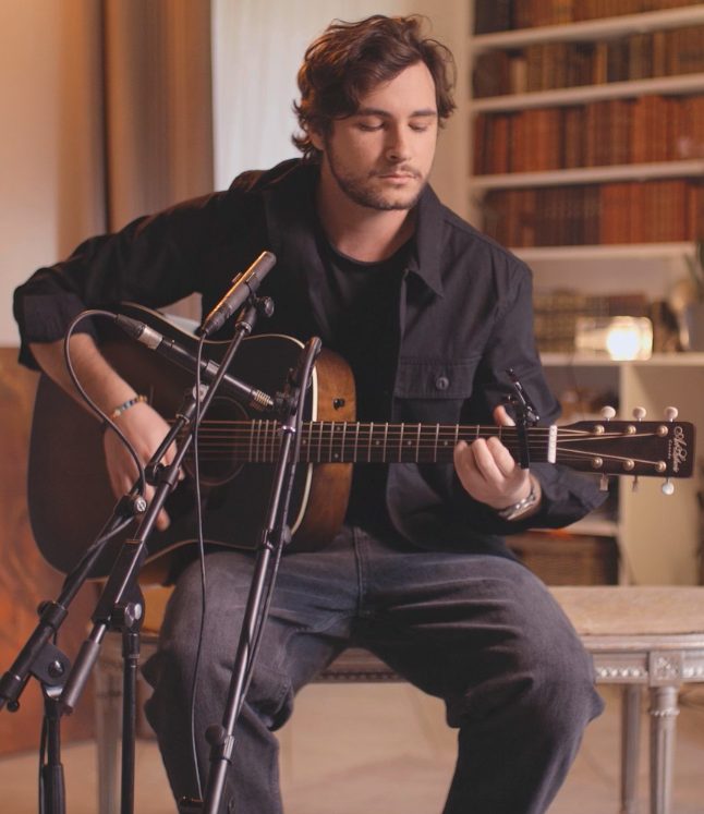 Côme joue de la guitare acoustique devant une bibliothèque